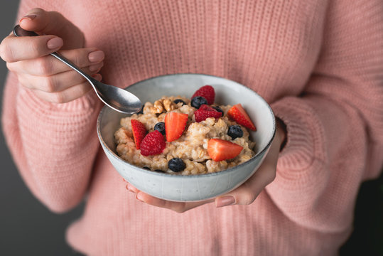 Woman in cozy pink sweater eating oatmeal porridge with berries. Concept of healthy eating, healthy lifestyle, dieting and weight loss. Vegan, vegetarian breakfast food