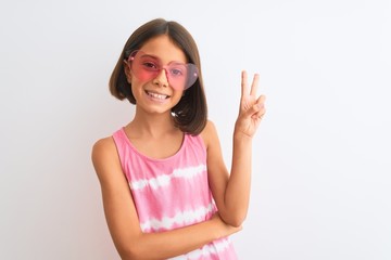 Young beautiful child girl wearing pink t-shirt and sunglasses over isolated white background smiling with happy face winking at the camera doing victory sign. Number two.