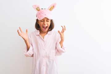 Beautiful child girl wearing sleep mask and pajama standing over isolated white background...