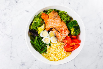 Healthy meal, keto food concept. Fish salad bowl on marble table background. Salad with salmon, couscous, vegetables, quail eggs. Top view, copy space