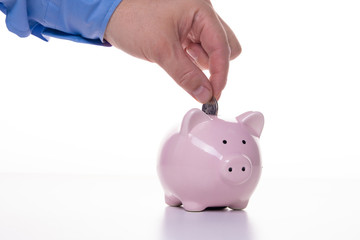 male hand puts a coin in a pink pig piggy bank on a white background. The concept of savings and savings, financial management