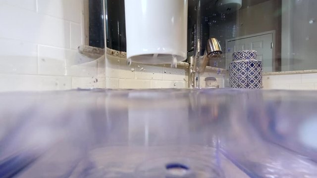 POV from inside clear pitcher as clean water drips from filter. Lens half submerged