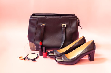 Makeup cosmetics, black shoes and black leather bag on pink background. Selective focus.