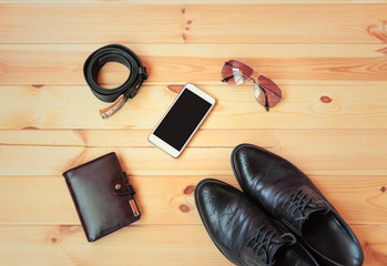 Fashionable black men's shoes, smartphone, wallet, sunglasses and  rolled belt on wooden background