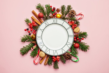 Flat lay composition with plate, winter fir branches, cones and Christmas decoration  on pink background. Copy space