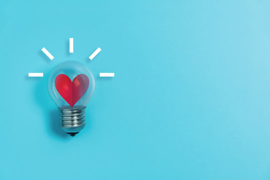 Red heart in light bulb on blue background with copy space.