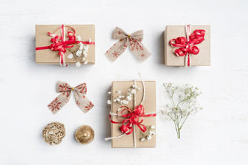 Christmas gifts with red ribbons, bows, gold pine cones and delicate white flowers on a rustic white background shot flat - lay.