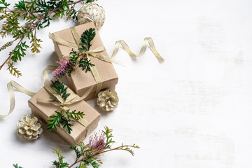 Australian inspired Christmas background. Gifts decorated with native Australia plant Grevillea and gold ribbon on a white background surrounded by cream pine cones and Grevillea foliage.
