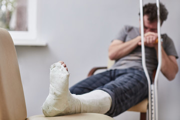 A sad man with a broken leg sits on a chair. Illness concept.