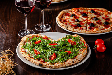 Italian food. Pizza for Valentine's Day for lovers in the form of a heart. Two glasses of red wine stand on the table. Romance in a restaurant for two. background image, copy space text