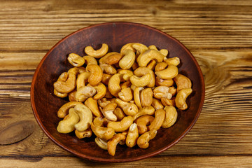 Ceramic plate with roasted cashew nuts on a wooden table