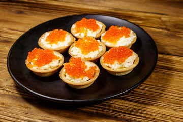 Tartlets with red caviar and soft cheese on a wooden table