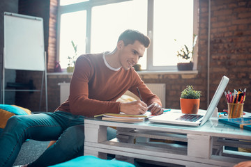 Handsome student smiling while enjoying studying process at home