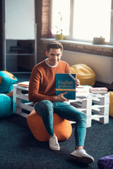 Student sitting in his cozy living room and holding English book