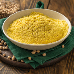 Chickpea flour in white ceramic bowl on wooden table close up