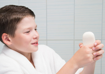 cheerful boy, in a white coat, in the bathroom, holds a bar of soap in his hand