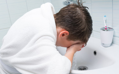 boy, in a white bathrobe, in the bathroom, washing his face under the tap, above the sink