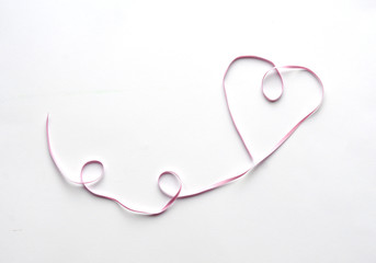 Pink ribbon shaped as heart on white table. Valentines Day background, copy space for text. Top view, flat lay. Love, wedding concept.