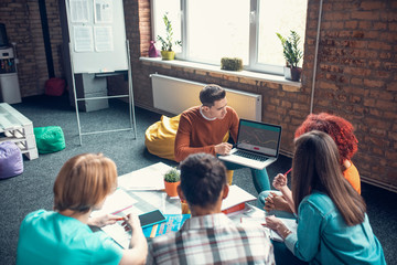 Student holding laptop and telling friends about project management