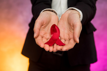 AIDS concept. Woman holding red ribbon in hands close up