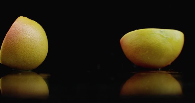 Slow motion. juicy grapefruit with drops and breaks into 2 slices with splashes on a glass table with reflection on a dark background