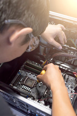 Male motherboard repairer using a screwdriver to replace the motherboard Concept of computer repair, close-up view of hardware - selective focus
