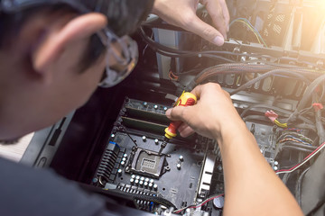 Male motherboard repairer using a screwdriver to replace the motherboard Concept of computer repair, close-up view of hardware