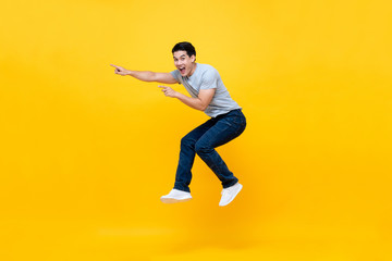 Energetic excited young Asian man in casual clothes jumping in yellow background