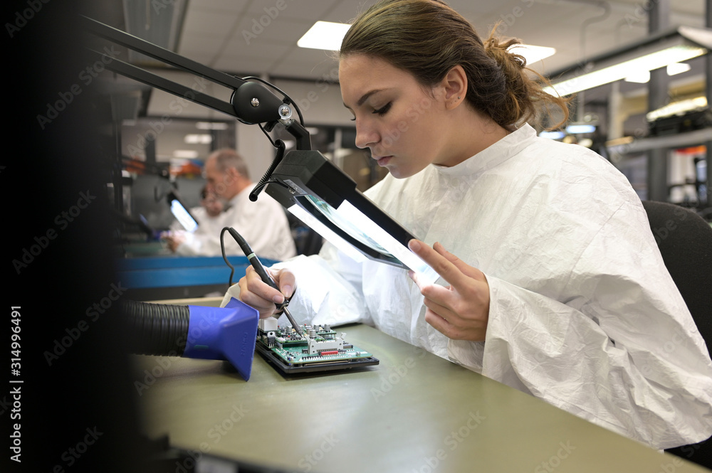 Wall mural Young woman apprentice working in microelectronics lab