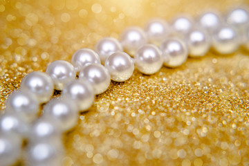 A necklace of pearls lies on a shiny gold background.
