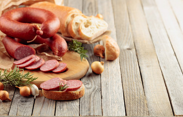 On a old wooden table sausage with bread, rosemary, onion and pepper.
