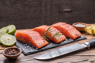 Fresh salmon fillets on black cutting board with herbs and spices.