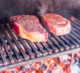 Steak cooking. Conceptual picture. Steak with spices and cutlery under burning grill grate.