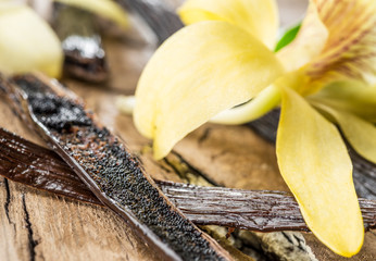 Dried vanilla fruits and vanilla orchid on wooden table.