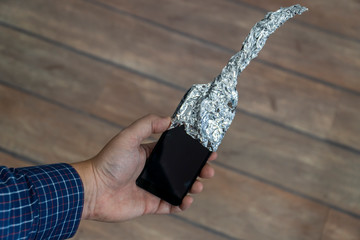 Hand holding phone covered in aluminum foil
