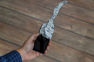 Hand holding phone covered in aluminum foil