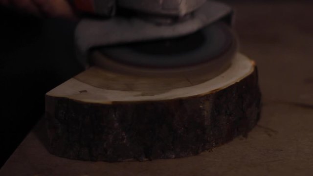 Close up of a carpenter using a handheld sander to smooth the face of a chopped, thick piece of wood, releasing sawdust