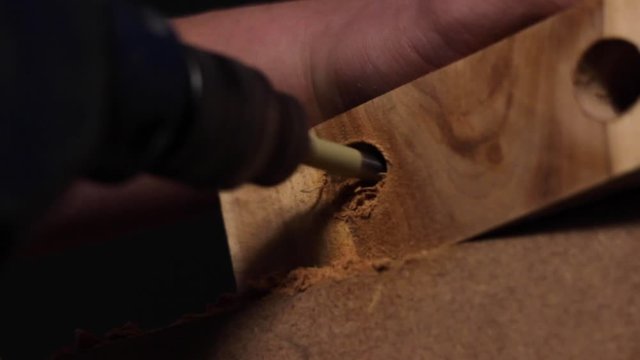 Close up of a carpenter using an electric drill to drill a hole into a slab of wood before retracting the tool, spraying sawdust everywhere