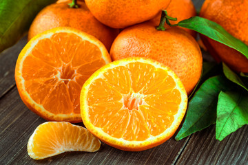 Ripe Mandarin fruit peeled open and place on old rustic look timber with group of mandarin fruits and leaves out of focus on the background