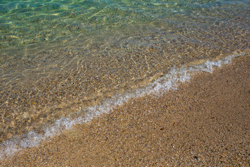 Beautiful transparent clear sea water splashing at sandy sunny beach of Greece. Horizontal color photography.