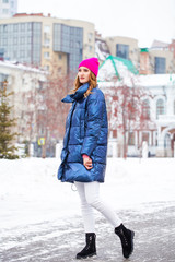 Young blonde woman in blue down jacket in winter street