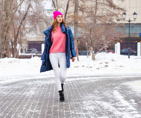 Young blonde woman in blue down jacket in winter street