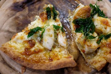 Close up a piece of seafood pizza on wooden table in a kictchen area