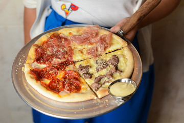 Waiter holds a plate with Italian four seasons pizza with different toppings, prosciutto, meat, olives, cheese, tomato