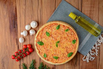 Colorful pizza ingredients: cherry tomatoes, basil, mushrooms, olive oil and pizza on wooden background. Copy space.