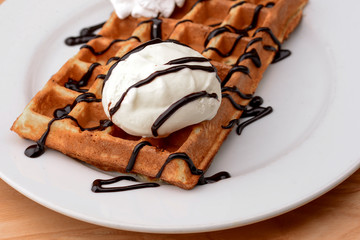 Plate of belgian waffles dessert with ice cream and chocolate caramel sauce on wooden table background.