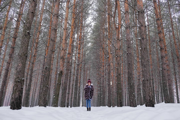 Portrait of a girl in a warm gray coat and burgundy knit scarf in the winter woods.