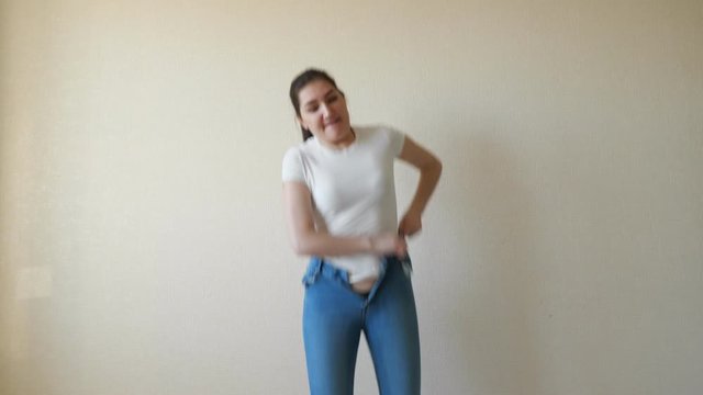 brunette struggles to pull on her jeans and can't button them.