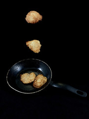 Potato pancakes in the cooking process. Fried pancakes in an old pan, on a black background. Cooked pies in a pan in oil.