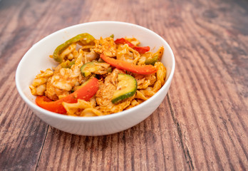  A white bowl of spicy chicken and pasta on a wooden background